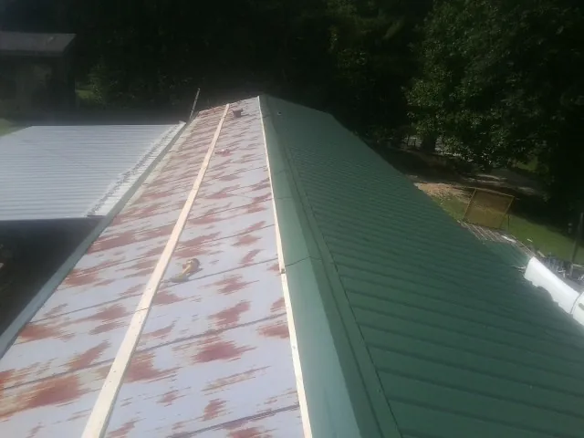 Old rusted panels beside newly installed green metal roofing — Wind Damage Roof Repair by Roofing Brothers in Blacksville