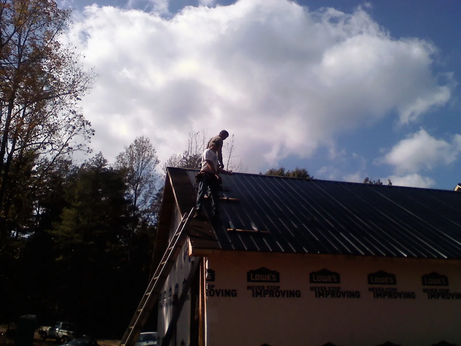 Roofer fastening dark metal panels high against a cloudy sky, from a Roof Inspection job in Blacksville