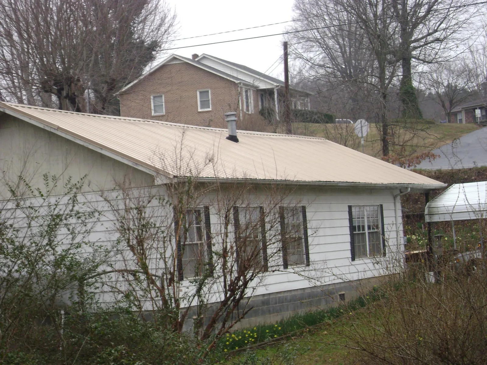 Tan metal roof on a white sided house set into a hillside — Commercial Roofing by Roofing Brothers in Blacksville